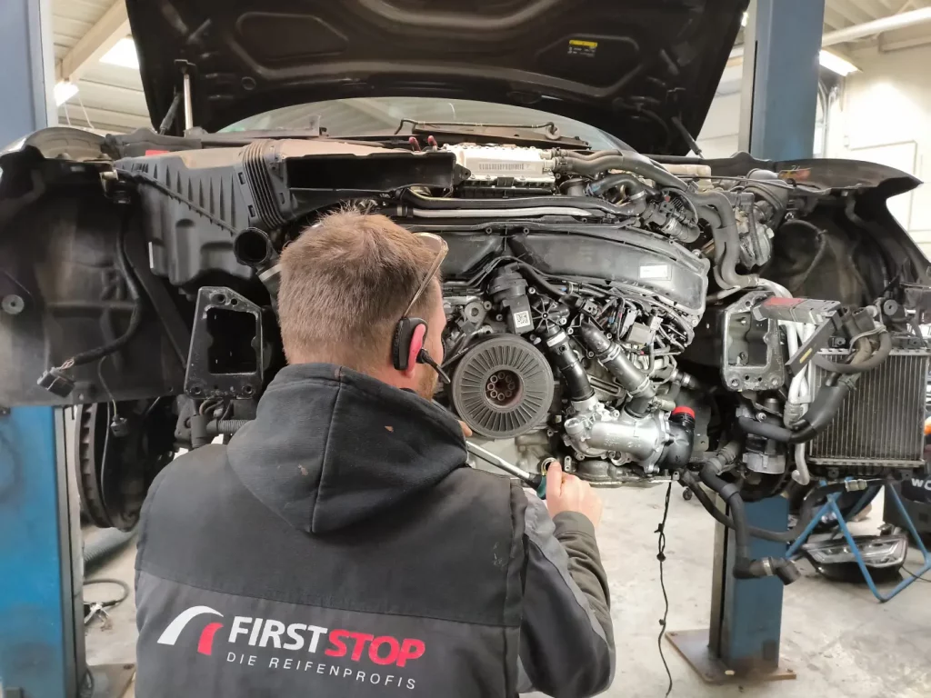 Mitarbeiter arbeitet am Fahrzeugmotor in der Werkstatt von FIRSTSTOP Schwerin. Fahrzeug auf Hebebühne.